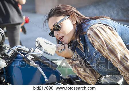 Stock Image - Woman applying makeup in motorcycle mirror. Fotosearch