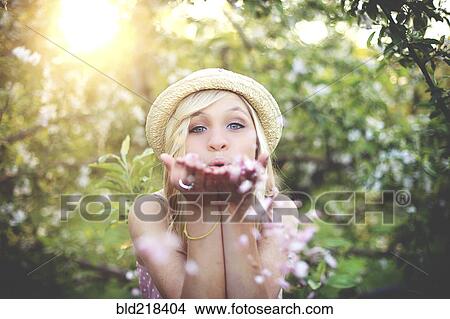 Picture - Woman blowing flower petals in garden. Fotosearch
