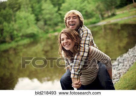 Stock Image - Woman carrying boyfriend piggyback near lake. Fotosearch