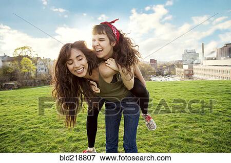 Woman carrying friend piggyback in urban park View Large Photo Image Stock Photo - Woman carrying friend piggyback in urban park. Fotosearch