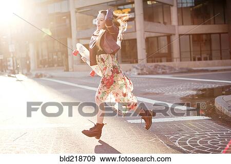 Stock Photo - Woman carrying skateboard in city intersection. Fotosearch