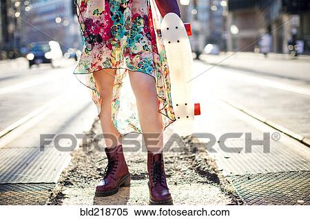 Stock Photography - Woman carrying skateboard on city sidewalk. Fotosearch