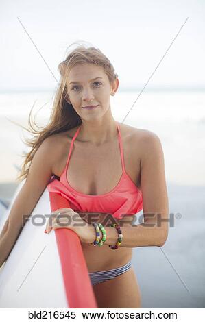 Stock Photography - Woman carrying surfboard on beach. Fotosearch