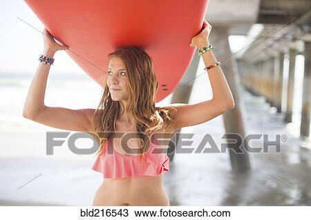 Woman carrying surfboard under boardwalk on beach View Large Photo Image Stock Image - Woman carrying surfboard under boardwalk on beach. Fotosearch