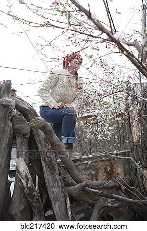 Stock Image - Woman climbing bare tree branches. Fotosearch