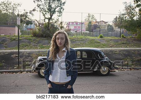 Stock Image - Woman crossing city street near classic car. Fotosearch