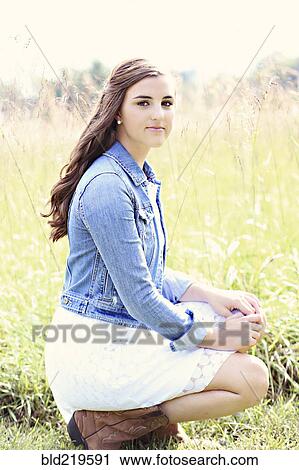 Stock Image - Woman crouching in tall grass in field. Fotosearch