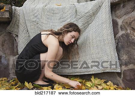 Stock Photo - Woman crouching under blanket near stone wall. Fotosearch