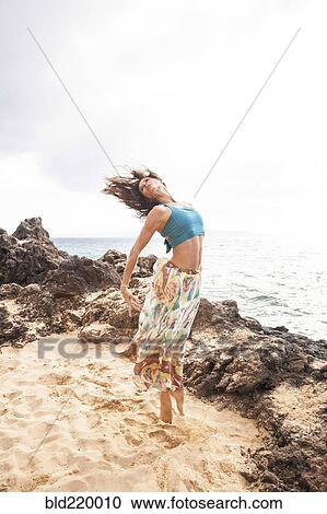 Stock Image - Woman dancing on rocky beach. Fotosearch