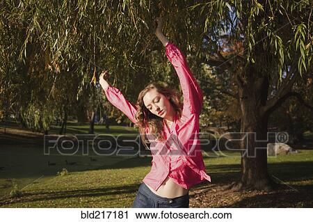 Stock Image - Woman dancing under tree in park. Fotosearch