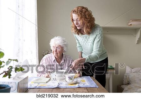 Stock Image - Woman feeding mother at table. Fotosearch