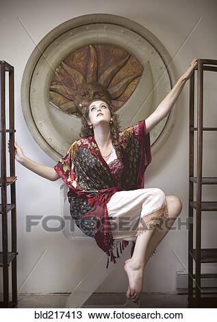 Stock Image - Woman floating between empty bookshelves in ornate room. Fotosearch