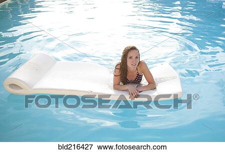 Stock Photo - Woman floating on raft in swimming pool. Fotosearch
