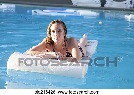 Stock Photograph - Woman floating on raft in swimming pool. Fotosearch