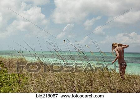 Stock Photo - Woman in bikini standing in beach grass. Fotosearch