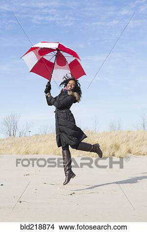 Picture - Woman in coat playing with umbrella on beach. Fotosearch