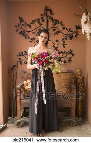 Stock Image - Woman in evening gown carrying bouquet of flowers. Fotosearch