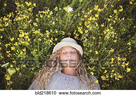 Stock Image - Woman in straw hat laying in flowers. Fotosearch