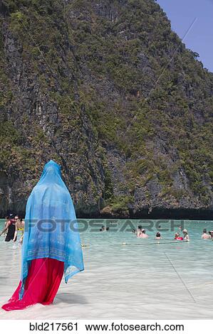 Stock Image - Woman in traditional headscarf standing on beach. Fotosearch
