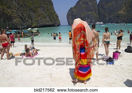 Stock Image - Woman in traditional headscarf standing on beach. Fotosearch