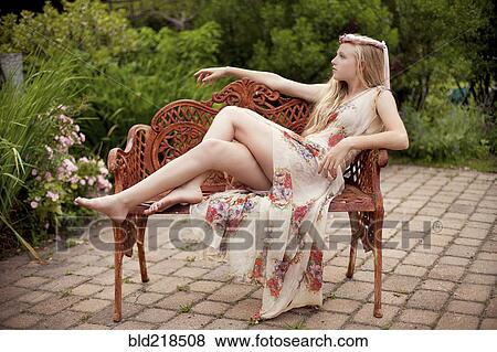 Stock Photo - Woman in wearing dress on bench in backyard. Fotosearch