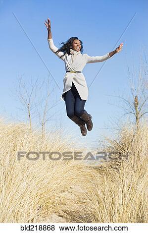 Stock Photo - Woman jumping for joy in beach grass. Fotosearch