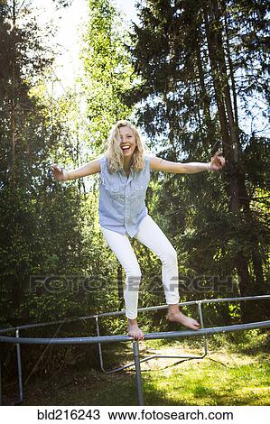 Stock Image - Woman jumping from metal structure in backyard. Fotosearch