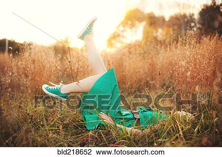 Stock Image - Woman laying in tall grass and kicking. Fotosearch