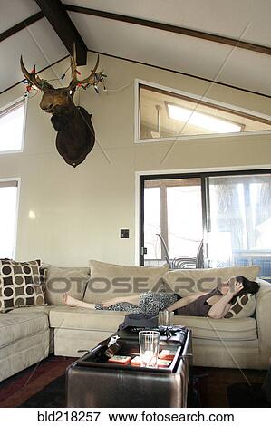 Stock Photo - Woman laying on sofa in living room. Fotosearch