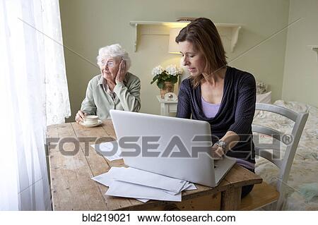 Stock Image - Woman paying bills for elderly mother. Fotosearch