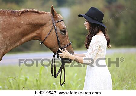 Stock Photo - Woman petting horse in rural field. Fotosearch