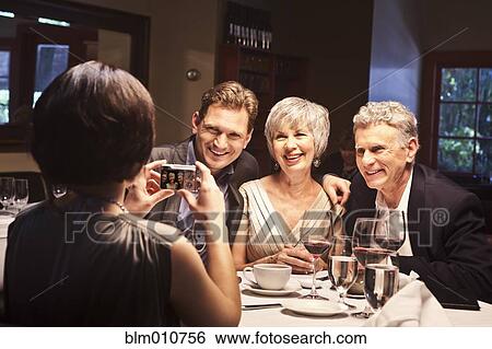 Woman photographing friends in restaurant View Large Photo Image Stock Photograph - Woman photographing friends in restaurant. Fotosearch