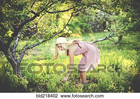 Stock Image - Woman picking flowers in rural field. Fotosearch
