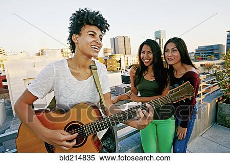 Stock Photography - Woman playing guitar for friends on urban rooftop. Fotosearch