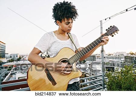 Stock Photo - Woman playing guitar on urban rooftop. Fotosearch