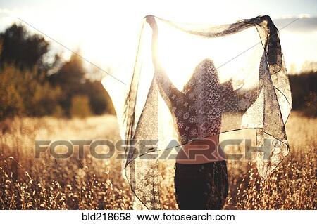Stock Photo - Woman playing with scarf in rural field. Fotosearch