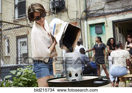 Picture - Woman pouring charcoal onto grill at barbecue. Fotosearch