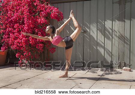 Stock Photo - Woman practicing yoga near flowers and fence. Fotosearch