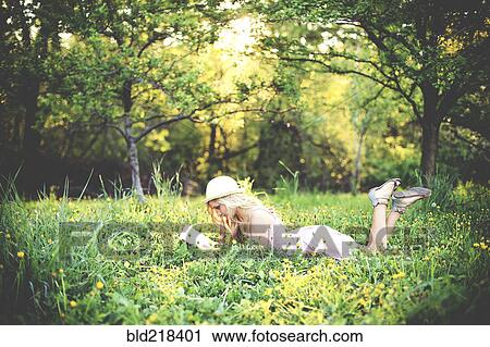 Stock Image - Woman reading book and laying in rural field. Fotosearch