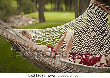 Stock Photo - Woman reading book in backyard hammock. Fotosearch