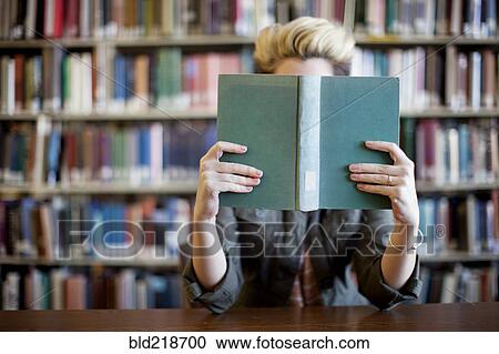 Stock Image - Woman reading book in library. Fotosearch