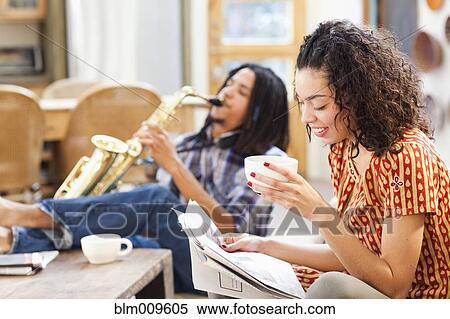 Stock Photography - Woman reading newspaper and listening to husband play saxophone. Fotosearch