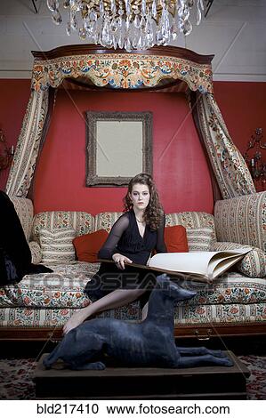 Stock Image - Woman reading oversized book on sofa in ornate living room. Fotosearch