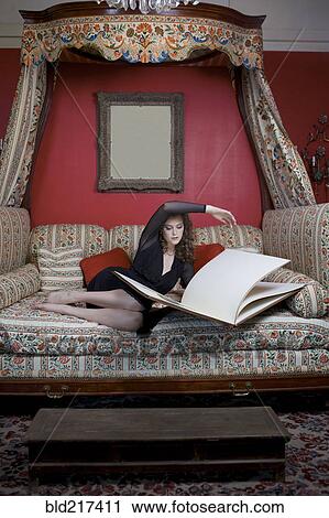 Stock Image - Woman reading oversized book on sofa in ornate living room. Fotosearch