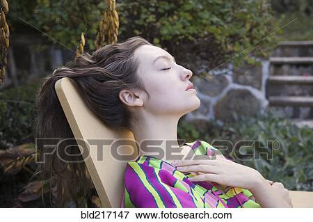 Stock Photo - Woman relaxing in lawn chair in backyard. Fotosearch