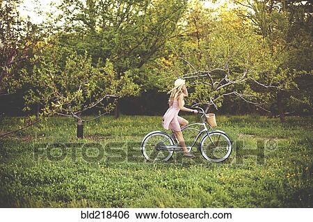 Stock Photograph - Woman riding bicycle in rural field. Fotosearch
