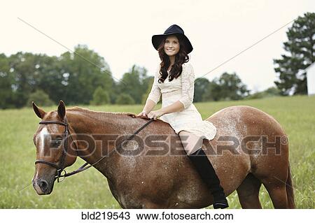Stock Image - Woman riding horse in rural field. Fotosearch