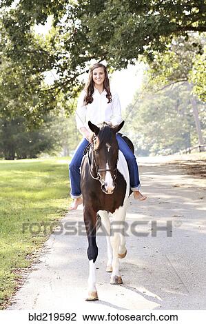 Stock Image - Woman riding horse on dirt road. Fotosearch
