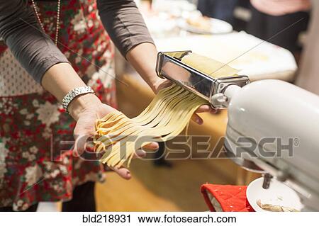 Stock Image - Woman rolling sheets of pasta in kitchen. Fotosearch