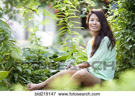 Stock Photo - Woman sitting in lush garden. Fotosearch